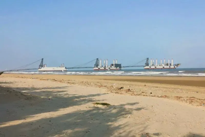 سفن ضخمة مرتبطة بجسور تمتد من شاطئ رملي إلى البحر، تعكس الابتكارات العسكرية الصينية وقدرتها على الهجوم البرمائي.