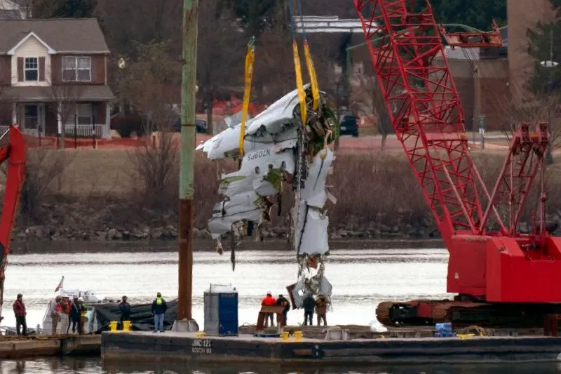 جهود انتشال الحطام من نهر بوتوماك، حيث يتم رفع جزء من الطائرة بواسطة رافعة، مع وجود فرق الإنقاذ في الموقع.