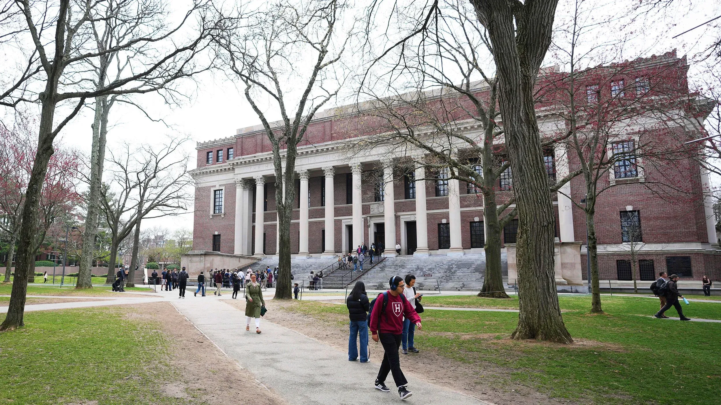 واجهة جامعة هارفارد التاريخية مع طلاب يتجولون في الحرم الجامعي، تمثل أهمية البحث الأكاديمي في التعليم العالي.