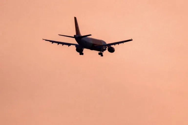 طائرة تحلق في السماء خلال غروب الشمس، تعكس التوترات الجيوسياسية في المنطقة بعد إغلاق المجال الجوي الإيراني.