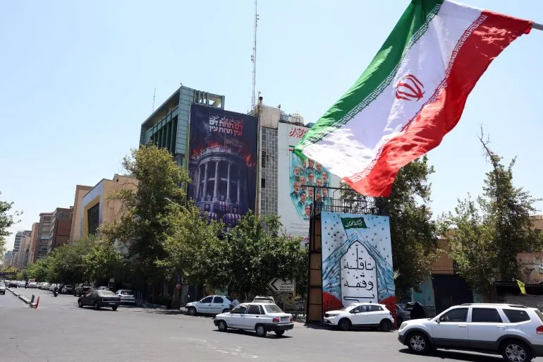 علم إيران يرفرف فوق شارع في طهران وسط توترات تصاعدية بين الولايات المتحدة وإيران بعد ضربات عسكرية مستمرة.