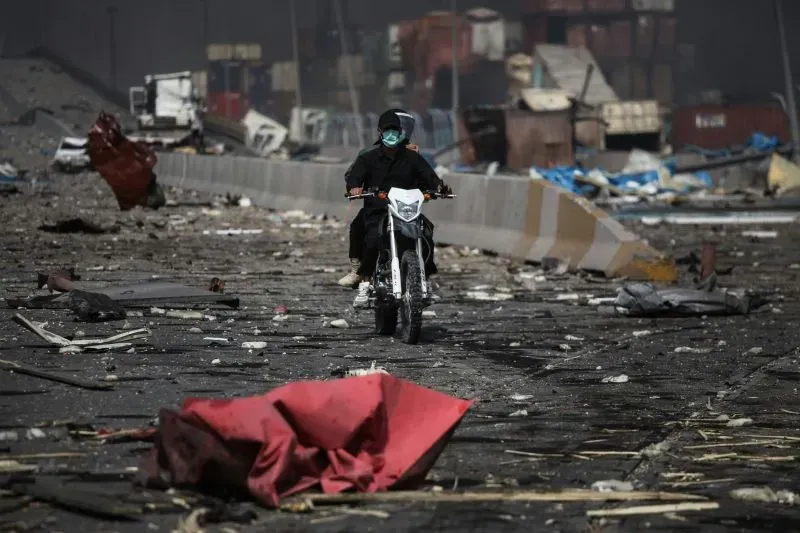 شخص يرتدي سترة داكنة وقناعاً، يقود دراجة نارية في ميناء بندر عباس، وسط حطام بعد الانفجار الكبير الذي أسفر عن مقتل 28 شخصًا.