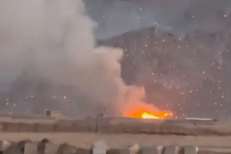 تصاعد الدخان والنيران في موقع هجوم جوي، مع تأثيرات واضحة على المنطقة المحيطة، مما يعكس تصاعد التوترات العسكرية بين إيران وإسرائيل.