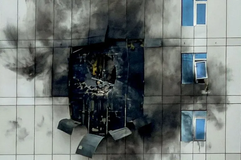 آثار دمار على واجهة مبنى نتيجة هجوم، مع تصاعد الدخان من الفتحة. تعكس الصورة تداعيات الهجمات الإيرانية في المنطقة.