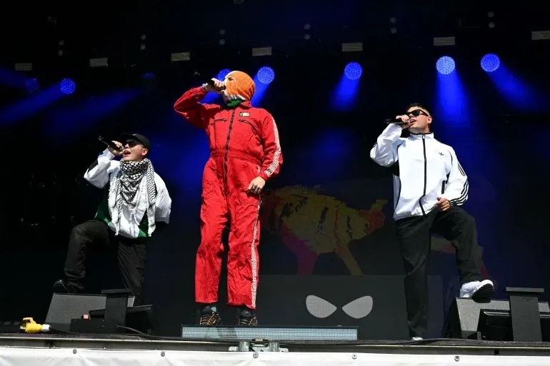 تظهر فرقة الراب الأيرلندية "كنيكاب" على المسرح في مهرجان غلاستونبري، حيث يرتدي الأعضاء الكوفية الفلسطينية ويؤدون أمام جمهور كبير.