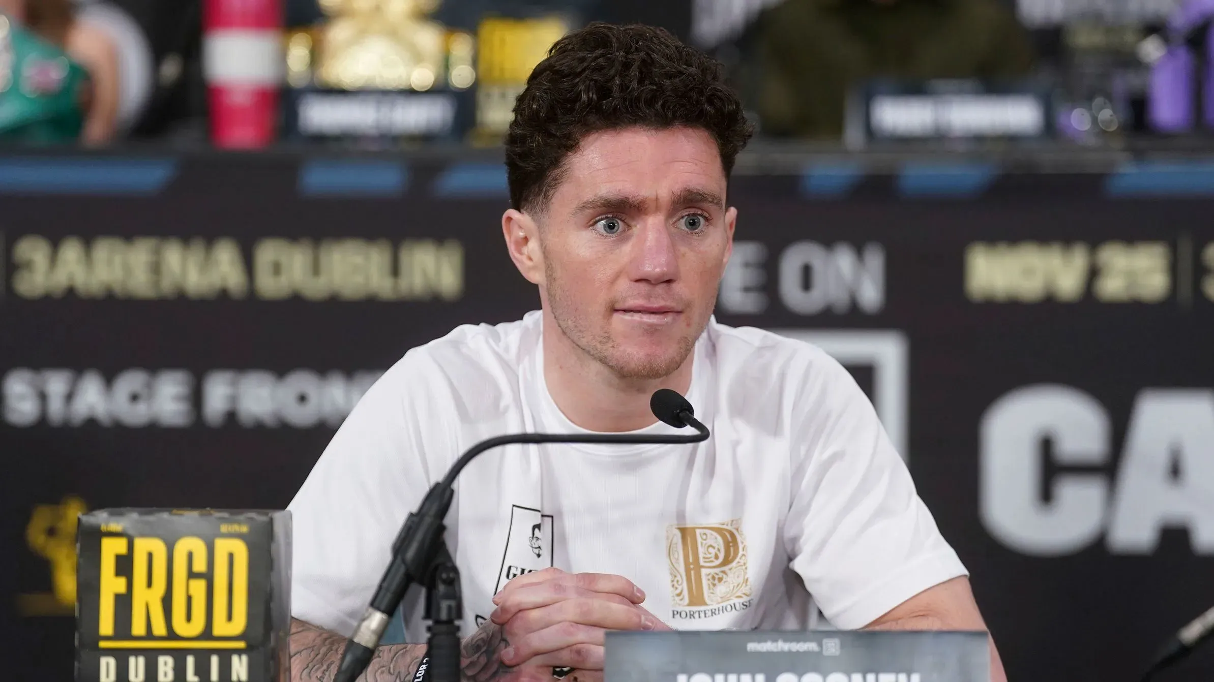 جون كوني، الملاكم الأيرلندي، يجلس في مؤتمر صحفي، مع تعبير وجهه يعكس الحزن بعد إصابته في نزال.