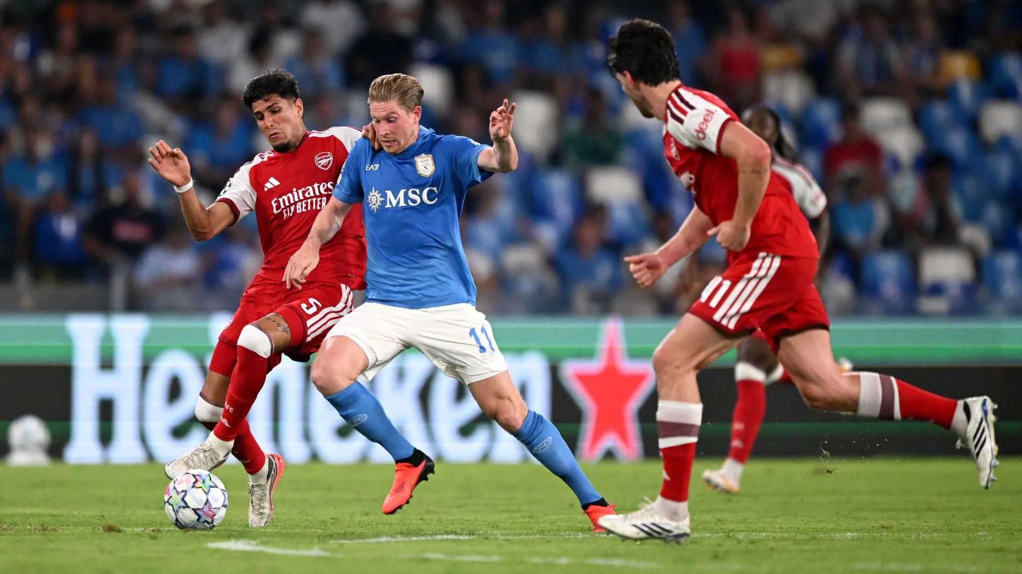 مباراة بين أرسنال ونابولي في دوري أبطال أوروبا، مع محاولة لاعب نابولي تخطي دفاع أرسنال وسط منافسة حامية.