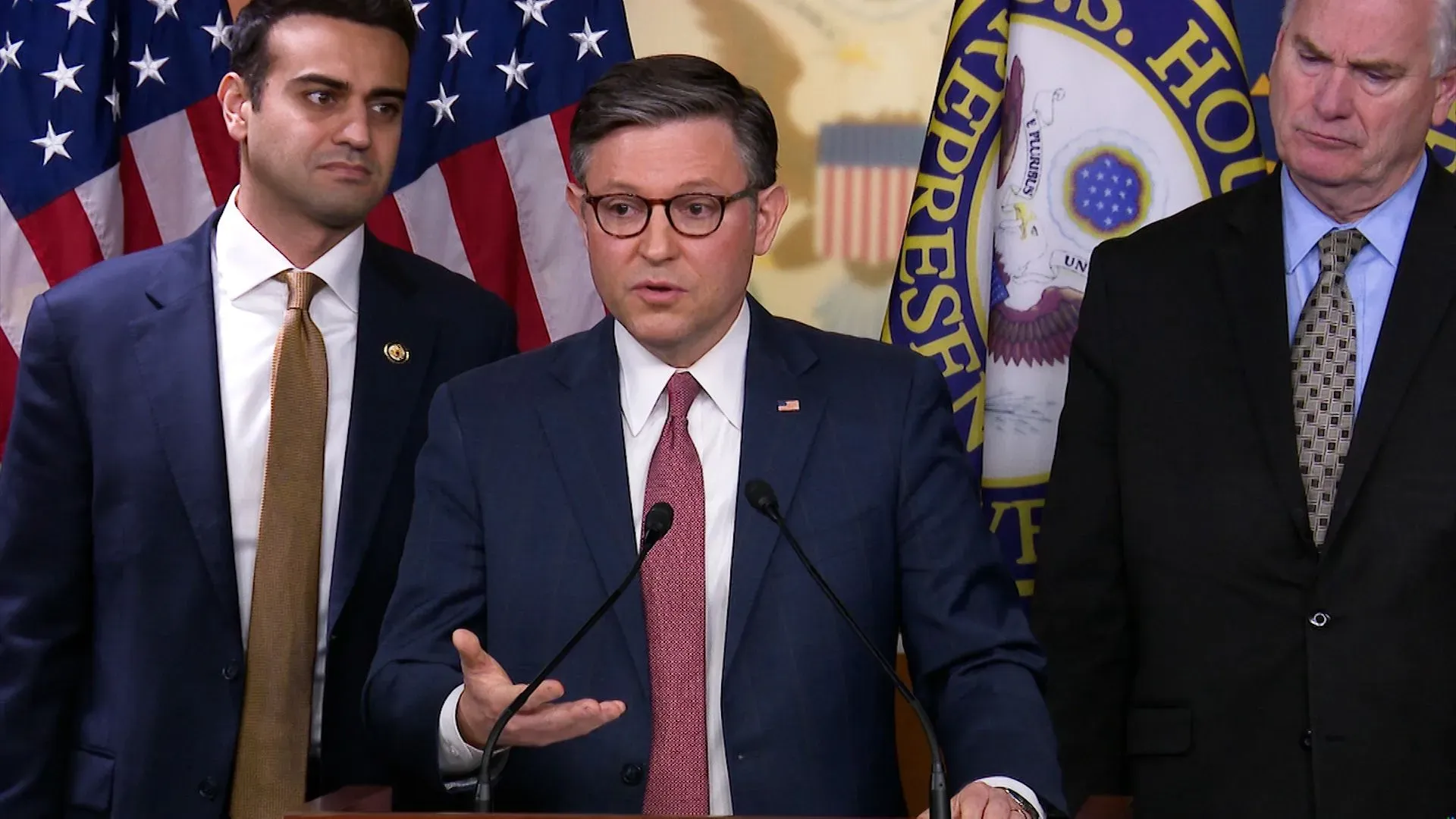 متحدثون في مؤتمر صحفي، مع أعلام الولايات المتحدة في الخلفية، يناقشون قضايا قانونية تتعلق بإقالات الرئيس ترامب للموظفين الفيدراليين.