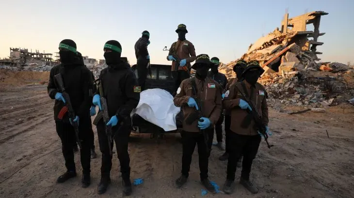 عناصر مسلحة من حماس يحملون تابوتًا في موقع مدمر، مما يعكس الوضع الإنساني المتدهور في غزة وسط استمرار النزاع.