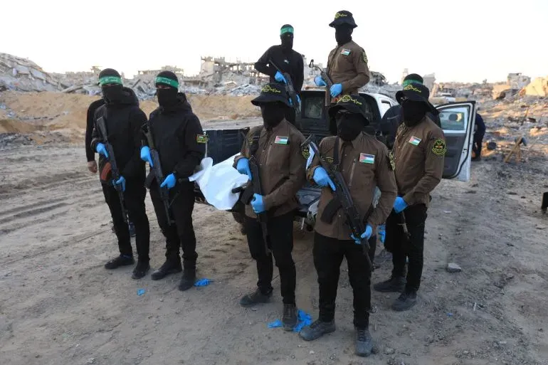 عناصر من حماس يرتدون ملابس عسكرية ويستعدون لنقل جثمان في منطقة مدمرة في غزة، في إطار جهود تسليم الجثث.