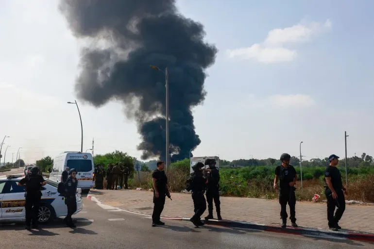 تصاعد دخان كثيف من موقع ضربة في هرتسيليا، بينما يتواجد أفراد من الشرطة الإسرائيلية في موقع الحادث.