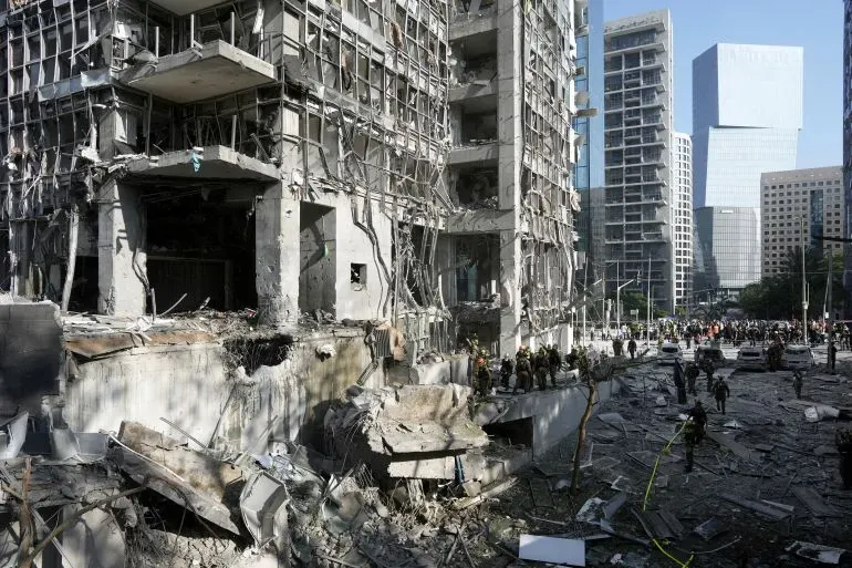 مبنى مدمر في إسرائيل بعد هجمات صاروخية، مع وجود فرق الإنقاذ في الموقع وأضرار كبيرة في الهيكل.