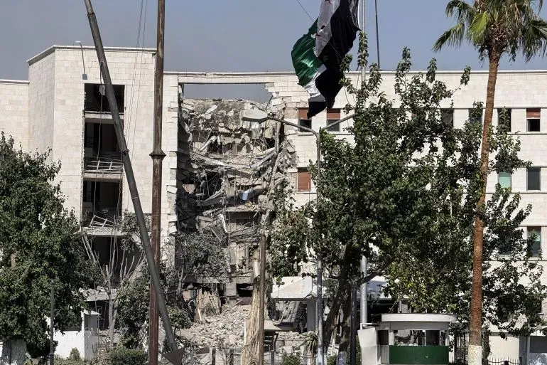 دمار كبير في مبنى في دمشق بعد الضربات الجوية الإسرائيلية، مع ظهور أعلام بين الأشجار، مما يعكس تصاعد التوترات في المنطقة.