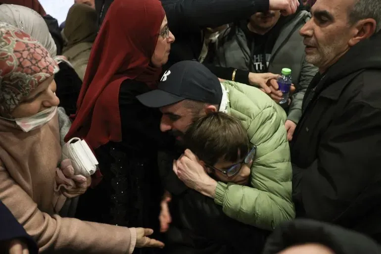 عائلة فلسطينية تتجمع في لحظة مؤثرة، حيث يحتضن الأب ابنه بينما تحيط بهم نساء وأشخاص آخرون، معبرة عن مشاعر الفقد والأمل في ظل الظروف الصعبة.