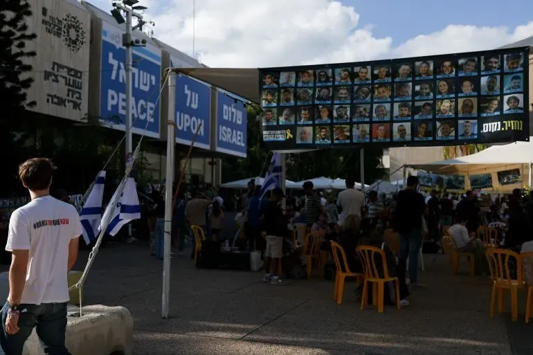 مظاهرة في تل أبيب لدعم الأسرى، حيث يظهر لافتات بأسماء الأسرى وصورهم، مع وجود حشد من الناس في الخلفية.