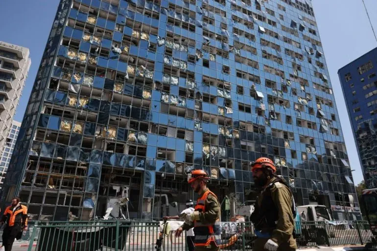 مبنى متضرر بشدة نتيجة الهجمات، مع نوافذ محطمة وأشخاص يرتدون زي الإنقاذ يتجولون في المنطقة.