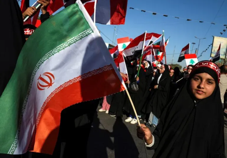 طفلة ترتدي الحجاب وتحمل علم إيران، وسط حشود من المتظاهرين الذين يحملون أعلامًا لبنانية وإيرانية في مسيرة دعم.