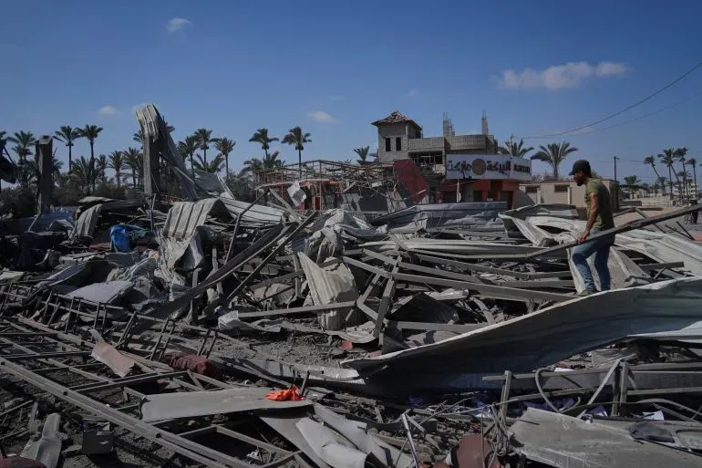 تظهر الصورة دمارًا واسعًا في دير البلح بقطاع غزة، مع شخص يتجول بين الأنقاض، مما يعكس آثار الهجمات الإسرائيلية على المدنيين.