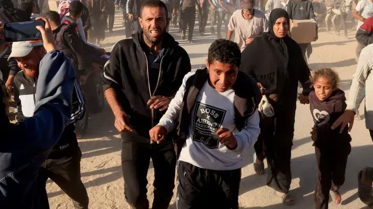 مشهد لمجموعة من الأشخاص، بينهم أطفال، يركضون في حالة من الفوضى بحثًا عن المساعدة أثناء قصف إسرائيلي في غزة، مما يعكس الوضع الإنساني المتدهور.