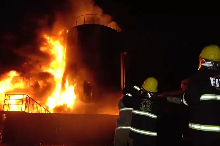 حريق هائل في منشأة صناعية بالحديدة، مع رجال الإطفاء يحاولون إخماد النيران، مما يعكس التوترات المتصاعدة في المنطقة.