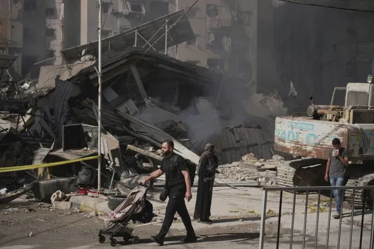 مشهد من الضاحية الجنوبية لبيروت يظهر دمارًا واسعًا بعد غارات إسرائيلية، مع شخص يدفع عربة طفل وسكان يتنقلون في المنطقة.