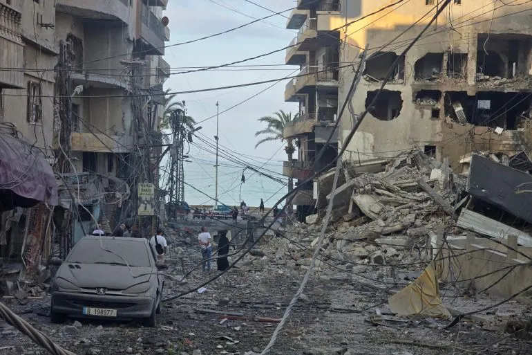 دمار واسع في منطقة سكنية بلبنان بعد الغارات الإسرائيلية، مع وجود أشخاص يتجولون بين الأنقاض وسيارة متضررة.