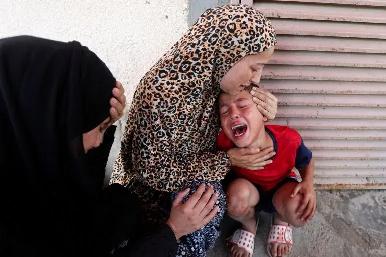 امرأة تعانق طفلاً يبكي، بينما تجلس امرأة أخرى بجانبهما، تعبيرات الحزن تعكس معاناة المدنيين في غزة وسط الأزمة الإنسانية.