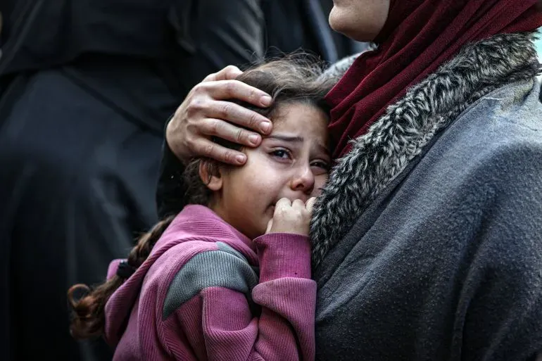 طفلة تبكي في حضن والدتها، تعكس مشاعر الحزن والقلق في ظل تصاعد العنف في غزة، حيث قُتل العديد من الفلسطينيين.