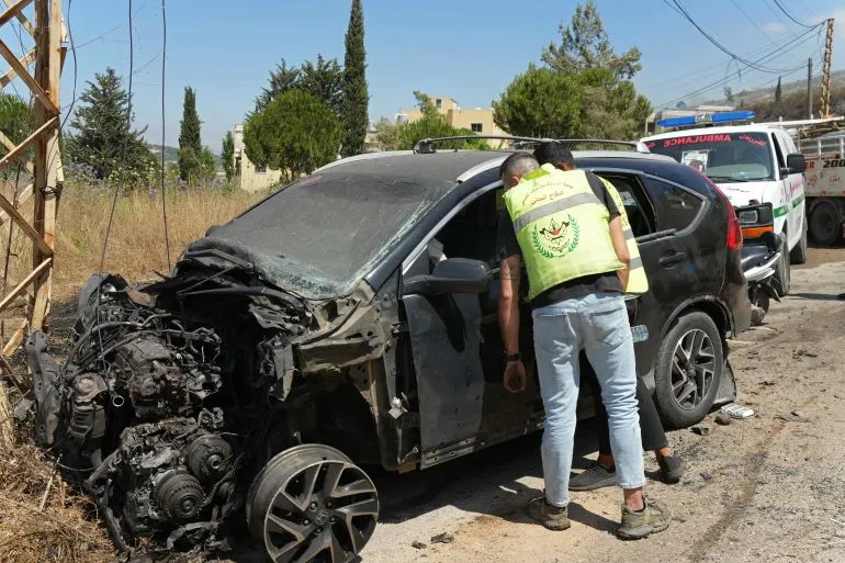 شخصان يفحصان سيارة متضررة بشدة في جنوب لبنان بعد ضربة جوية إسرائيلية ضمن تصاعد الهجمات العسكرية المستمرة.