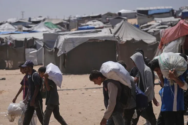 مجموعة من الأطفال والبالغين يحملون أمتعة أثناء مغادرتهم مخيم للاجئين في غزة، في ظل ظروف قاسية بحثًا عن المساعدات الإنسانية.