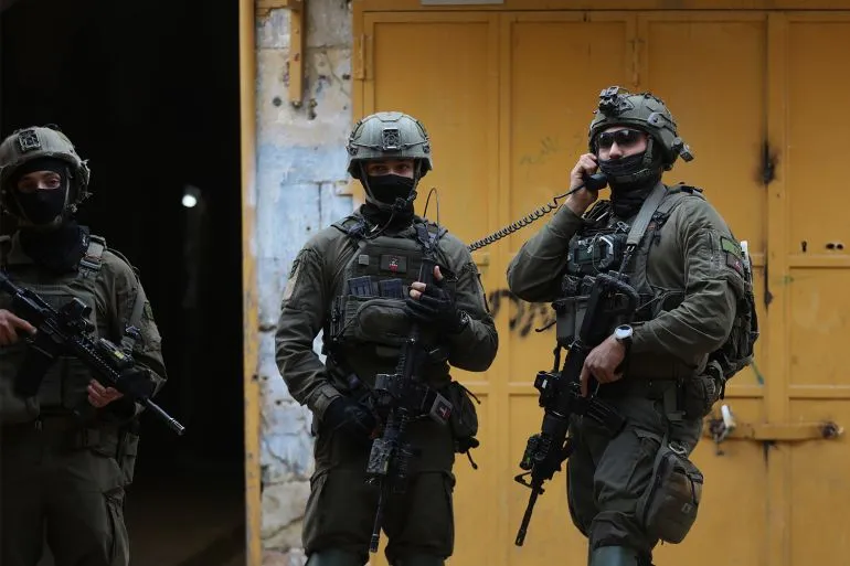 جنود إسرائيليون مدججون بالسلاح يقفون في شارع ضيق، مع خلفية جدران ملونة، في سياق تصعيد التوترات في الضفة الغربية المحتلة.