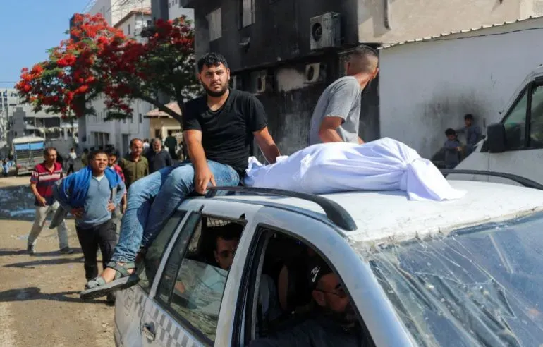 شبان فلسطينيون يجلسون على سطح سيارة في غزة، مع غطاء أبيض يظهر على السطح، في أعقاب الهجمات الإسرائيلية التي أسفرت عن العديد من الضحايا.