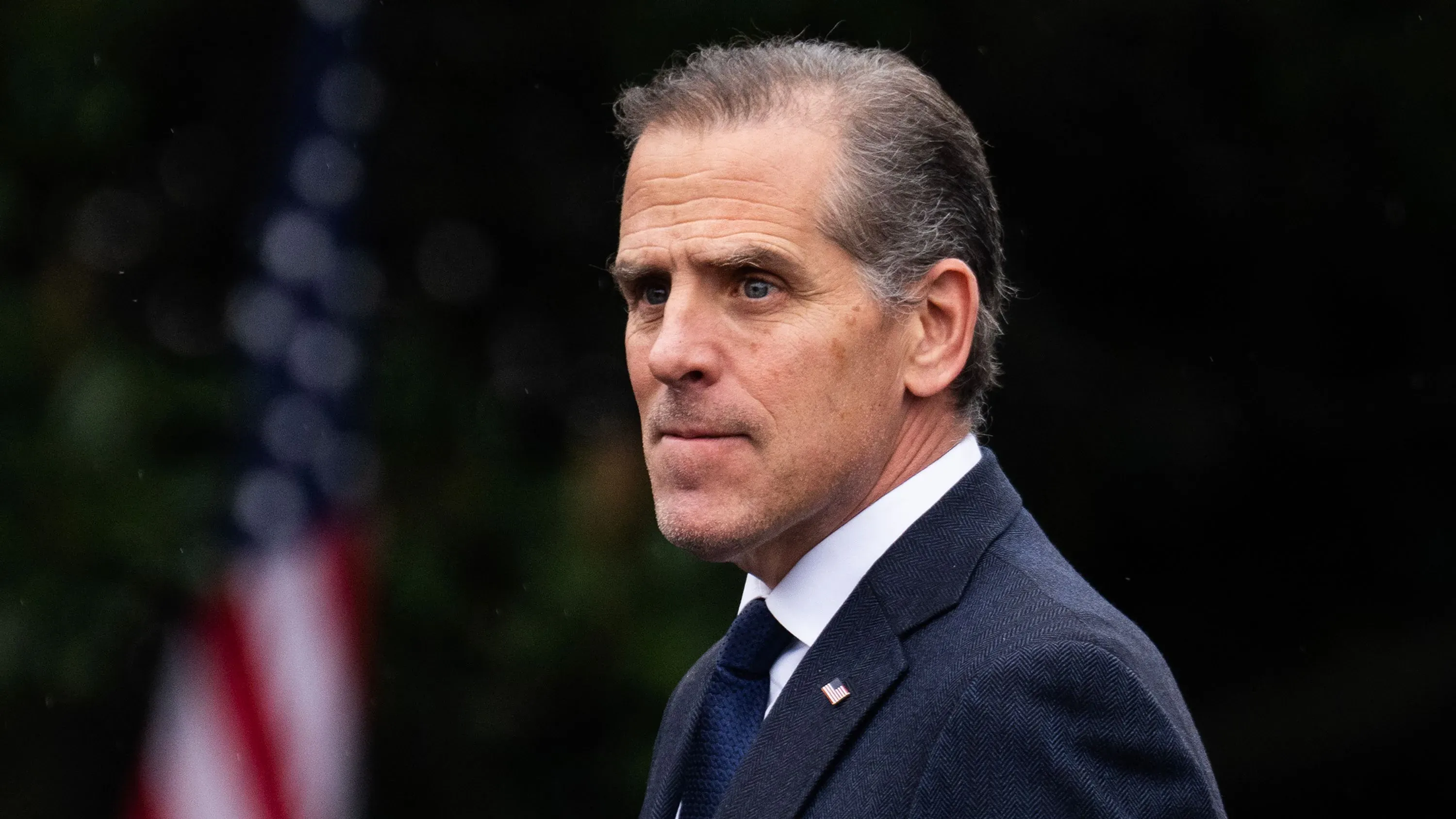 يظهر هانتر بايدن وهو ينظر بجدية، مع العلم الأمريكي في الخلفية، في سياق التحقيقات الجارية حول عائلته.