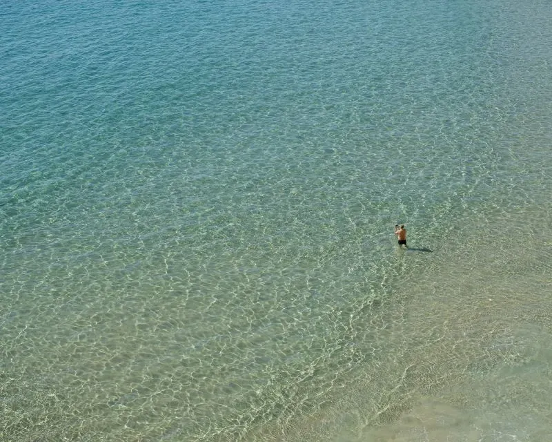 طفل يقف في المياه الصافية لشاطئ بينيدورم، مع تدرجات زرقاء تعكس جمال السياحة في المدينة.