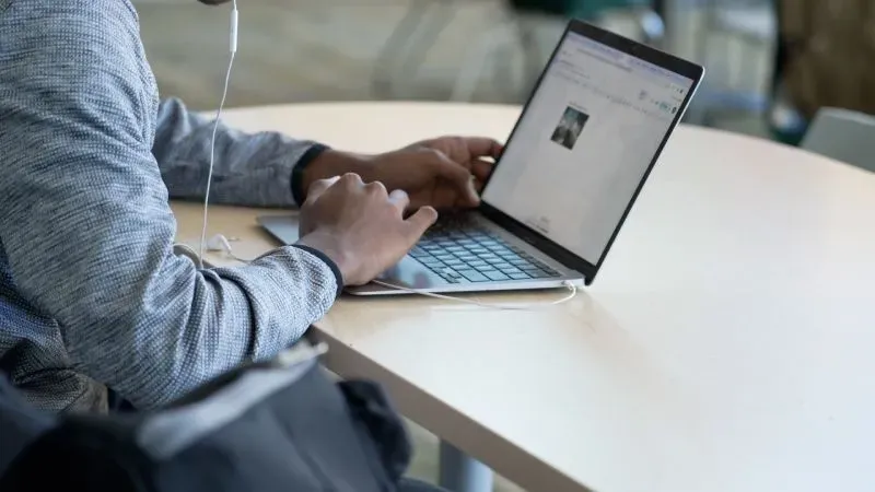 طالب يستخدم جهاز كمبيوتر محمول للدراسة في فصل دراسي، مع التركيز على التعليم بعد تطبيق سياسة حظر الهواتف في المدرسة.