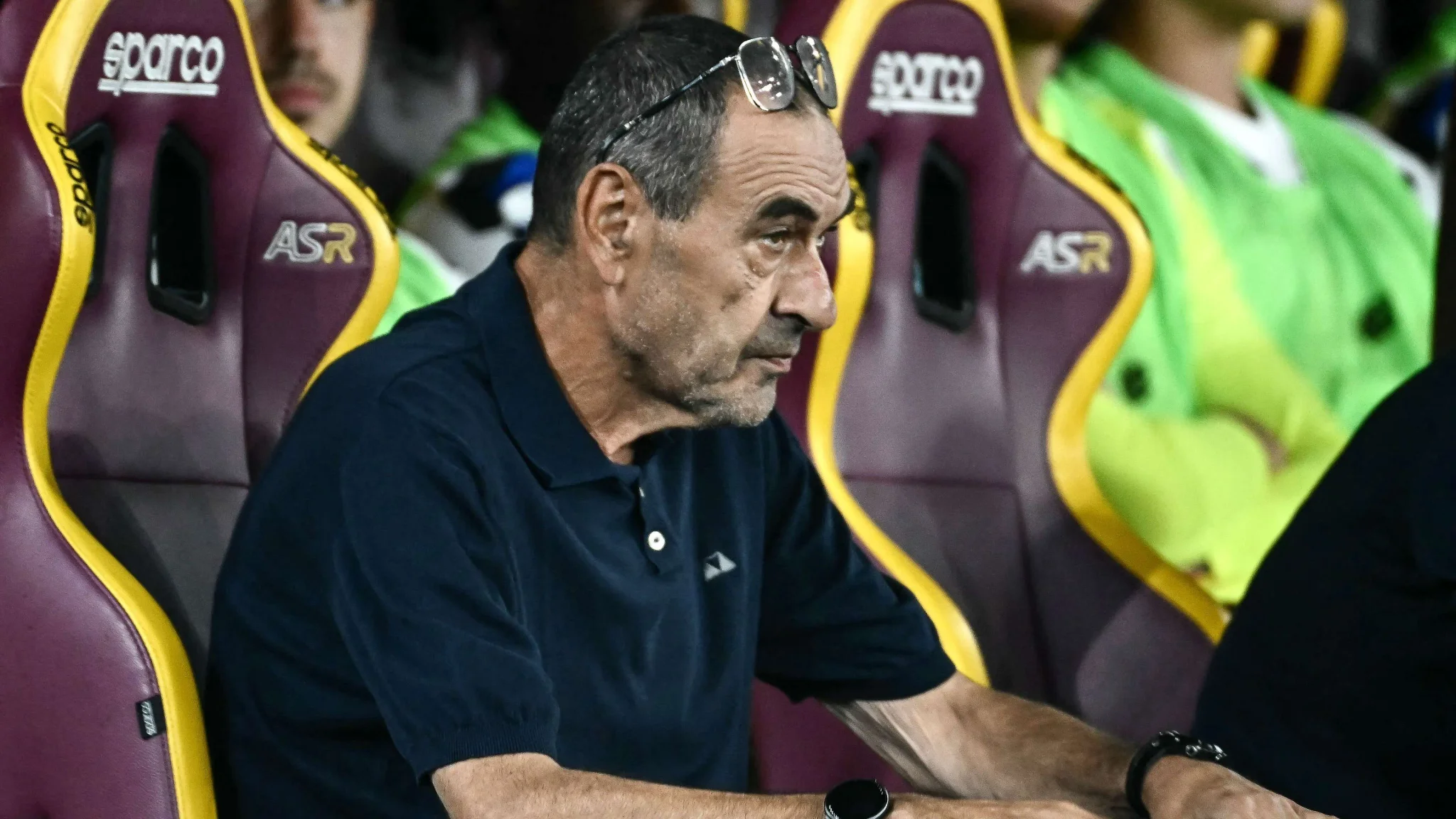 المدرب ماوريتسيو ساري جالس على مقعد بدلاء فريق أتالانتا خلال مباراة في الدوري الإيطالي، مع التركيز على تعبيره الجاد وخبرته في كرة القدم.