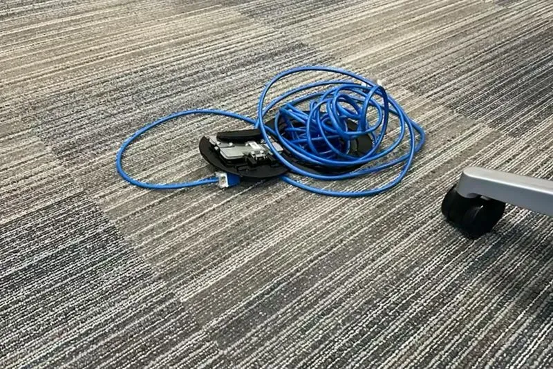 سلك أزرق متشابك مع جهاز صغير على أرضية مكتبية، يعكس الفوضى الناتجة عن تخفيضات الحكومة وتأثيرها على الموظفين الفيدراليين.