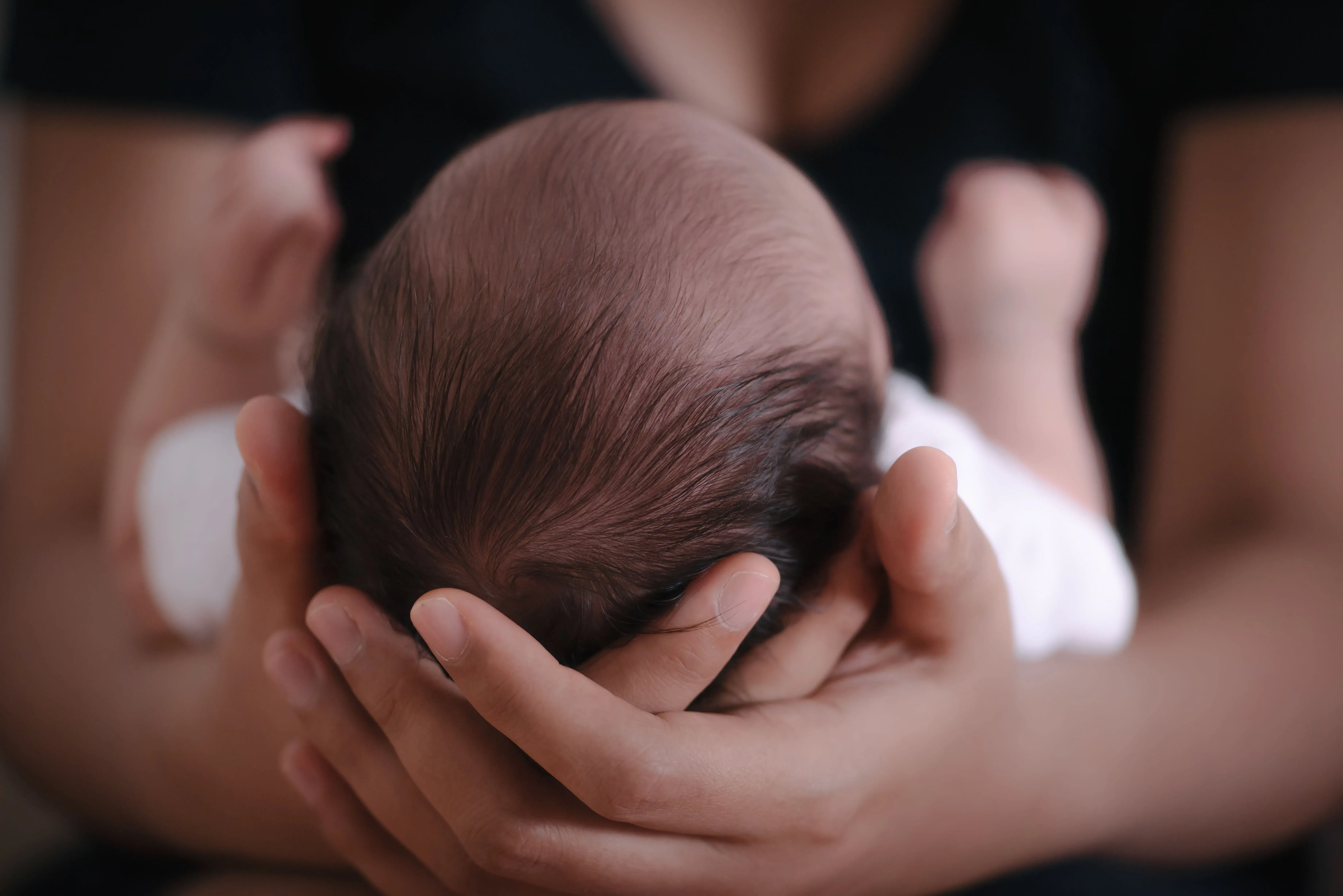 رأس طفل حديث الولادة في يد شخص بالغ، مما يعكس أهمية حقن فيتامين K لحماية الأطفال من النزيف الخطير.