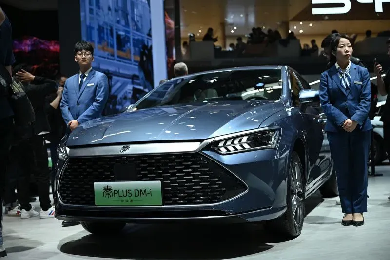 سيارة BYD PLUS DM-i الجديدة معروضه في معرض، بجانب موظفين يرتدون زي رسمي، مما يعكس الابتكار والتقدم في صناعة السيارات الكهربائية.