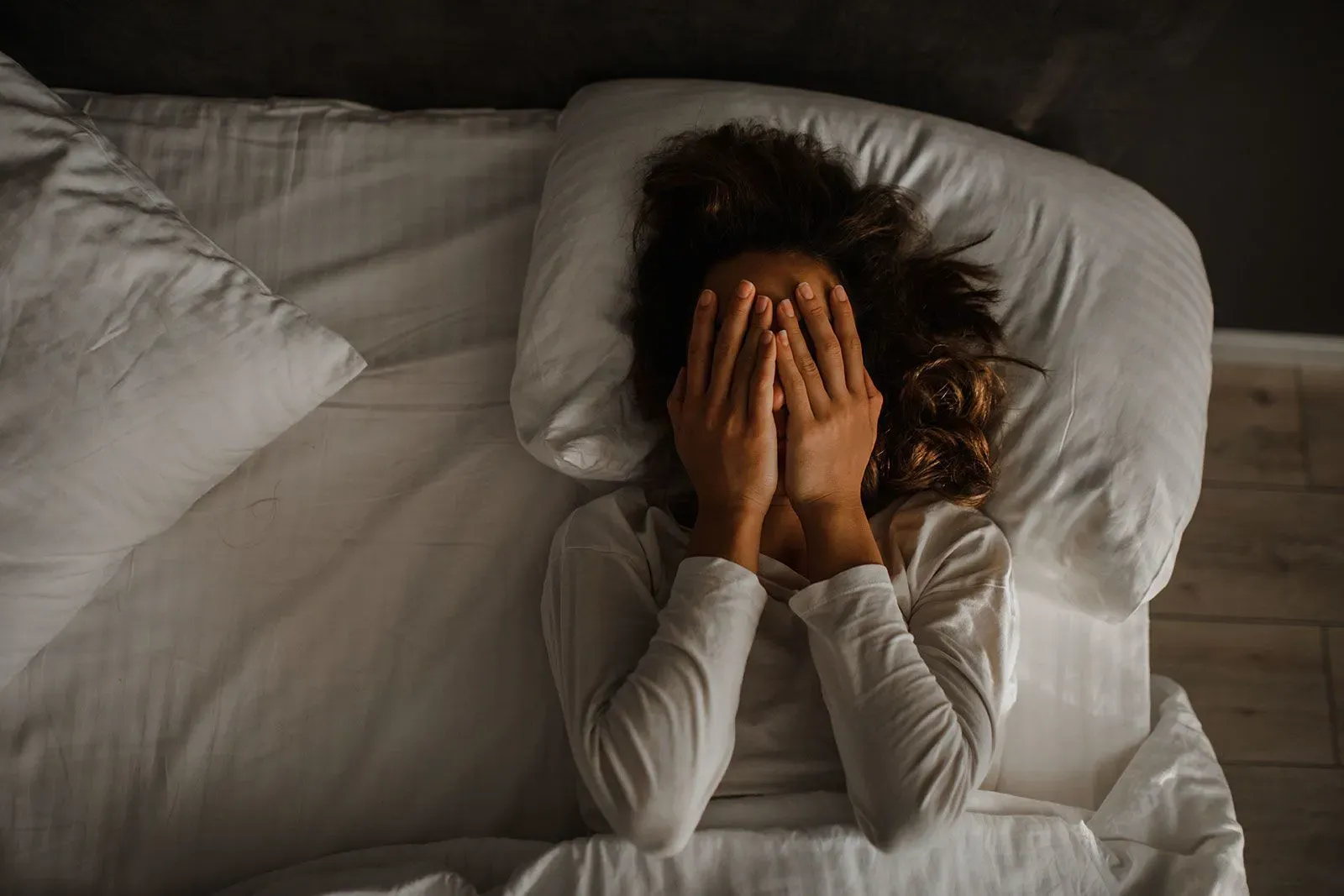 امرأة في السرير تغطي وجهها بيديها، تعبر عن الإحباط بسبب الأرق وتأثيره على الصحة العقلية.