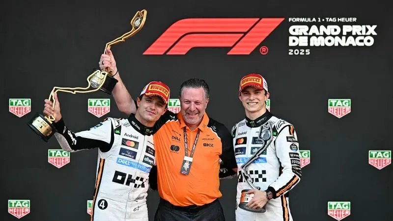 نوريس وبياستري يحتفلان بفوزهما في سباق جائزة موناكو الكبرى 2025 مع مدير فريق مكلارين، مع وجود شعار الفورمولا 1 في الخلفية.