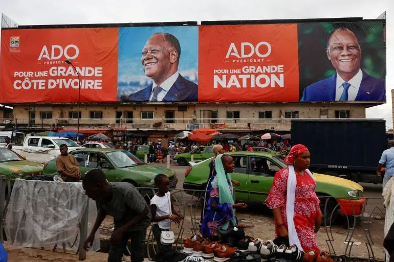 لافتة انتخابية كبيرة تظهر صورة الرئيس الحسن واتارا مع عبارة "من أجل كوت ديفوار عظيمة" في وسط مدينة أبيدجان، مع وجود أشخاص ومركبات في الخلفية.