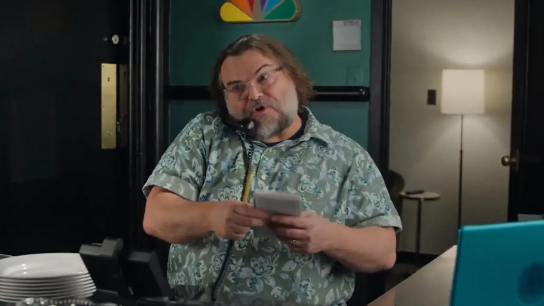 جاك بلاك يتحدث في الهاتف أثناء التحضير لاستضافة برنامج "ساترداي نايت لايف"، مرتديًا قميصًا مزخرفًا، في خلفية استوديو 8H.