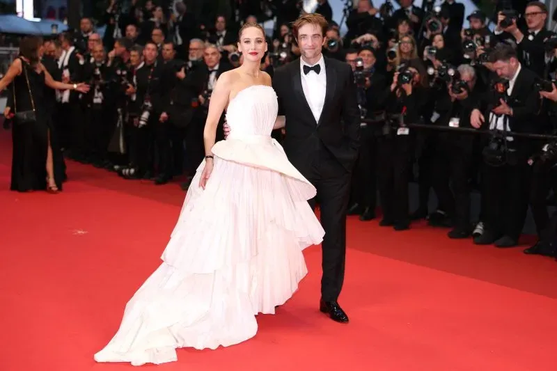 نجمان يتألقان على السجادة الحمراء لمهرجان كان السينمائي، وسط حشد من المصورين. الأجواء تحتفل بالفن والسينما.