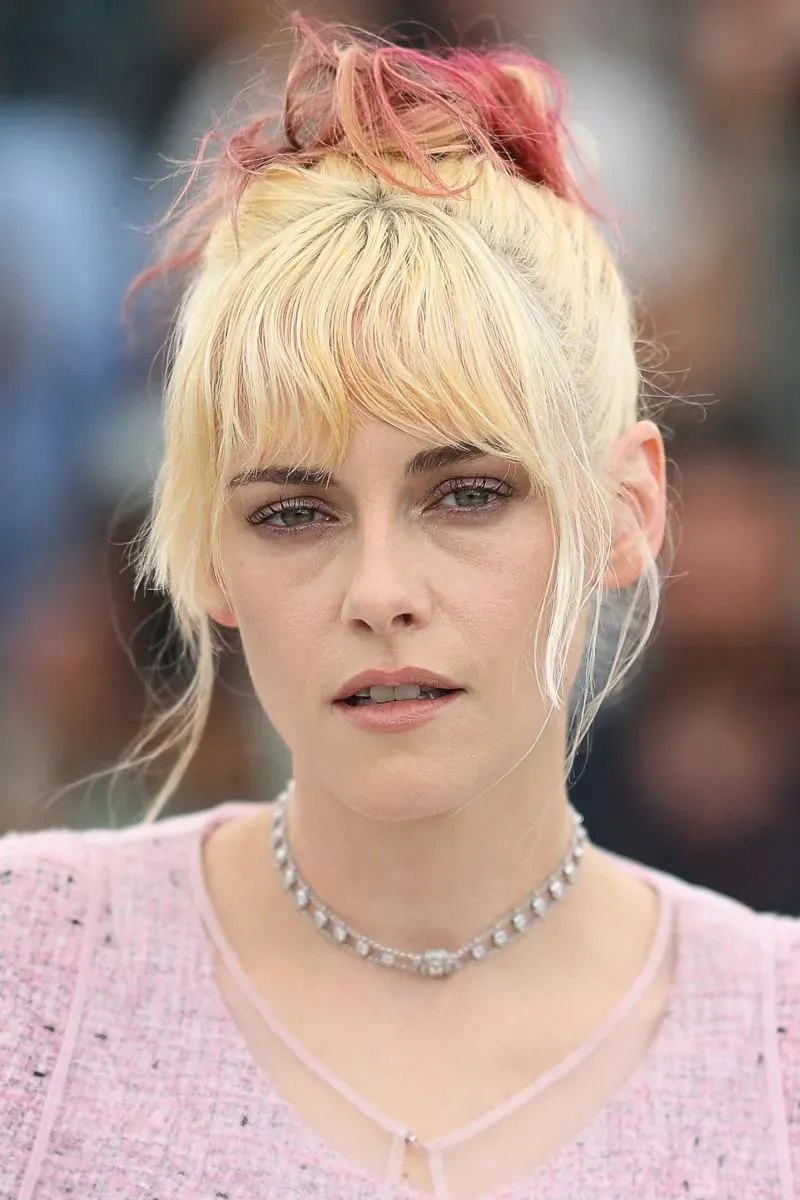 صورة قريبة لوجه ممثلة ترتدي ملابس وردية ولها شعر أشقر مع خصلات وردية، تعكس أجواء مهرجان كان السينمائي.