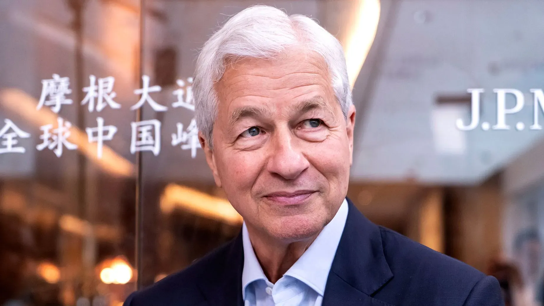 جيمي ديمون، الرئيس التنفيذي لبنك JPMorgan Chase، يتحدث في قمة في الصين، مع خلفية تحمل اسم البنك، مشيرًا إلى المخاطر الاقتصادية الحالية.
