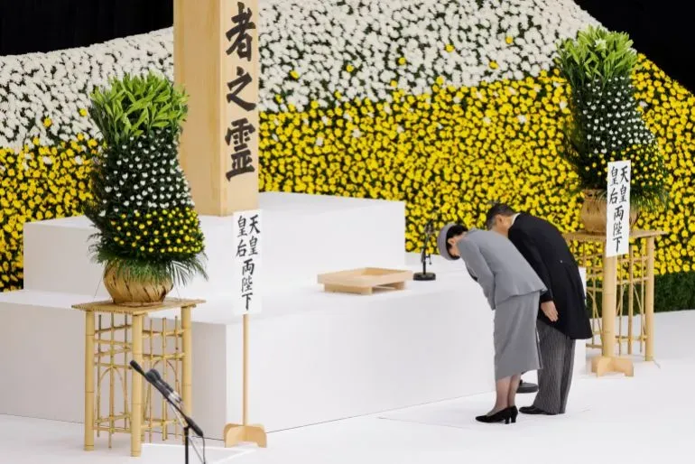 إمبراطور اليابان ناروهيتو وزوجته يقدمان الاحترام في مراسم إحياء ذكرى قتلى الحرب، مع خلفية من الأزهار الملونة.