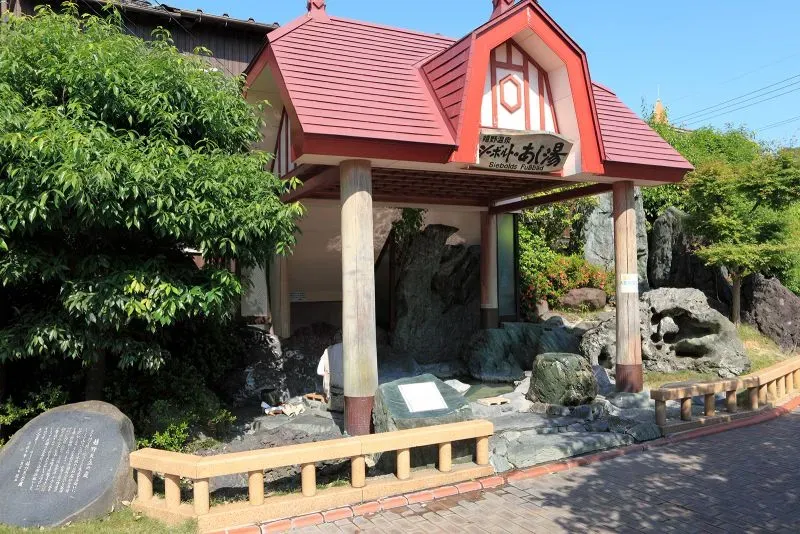 مدخل حوض الأونسن في أوريشينو، يحيط به نباتات خضراء وصخور، يُظهر تأثير السياحة على الينابيع الساخنة في اليابان.