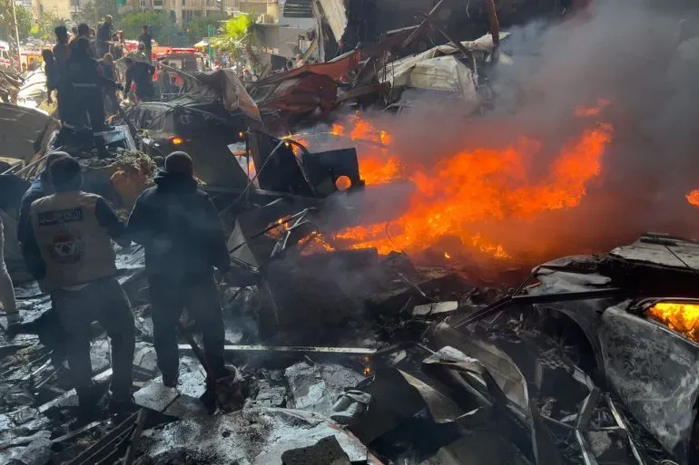 دخان يتصاعد من حطام مبنى بعد هجوم إسرائيلي في لبنان، حيث يتجمع رجال الإنقاذ وسط الفوضى. الهجوم أسفر عن مقتل وإصابة العشرات.