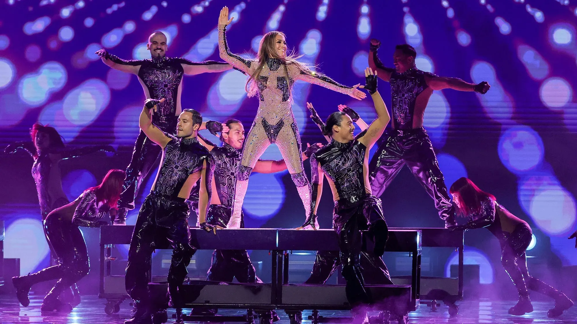 جينيفر لوبيز تؤدي عرضًا مميزًا مع راقصين على خشبة المسرح، محاطة بأضواء ملونة، في إعلان عن حفلاتها في لاس فيغاس.